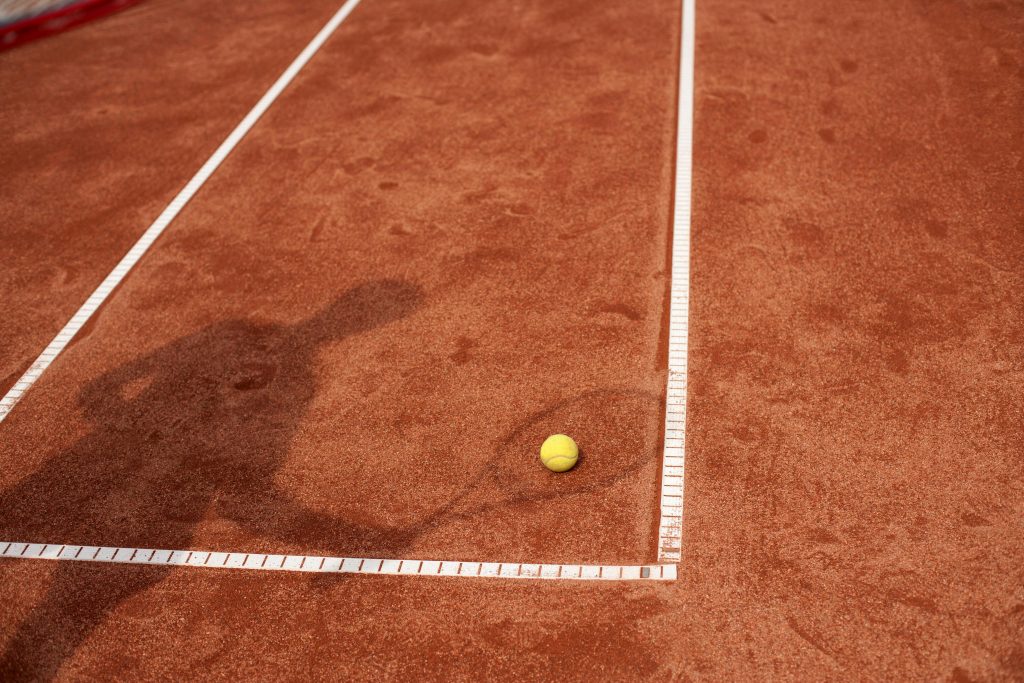 pexels photo 12645021 12645021 Shadow of a tennis player on a clay court with a yellow tennis ball. Perfect for sports and tennis themes.