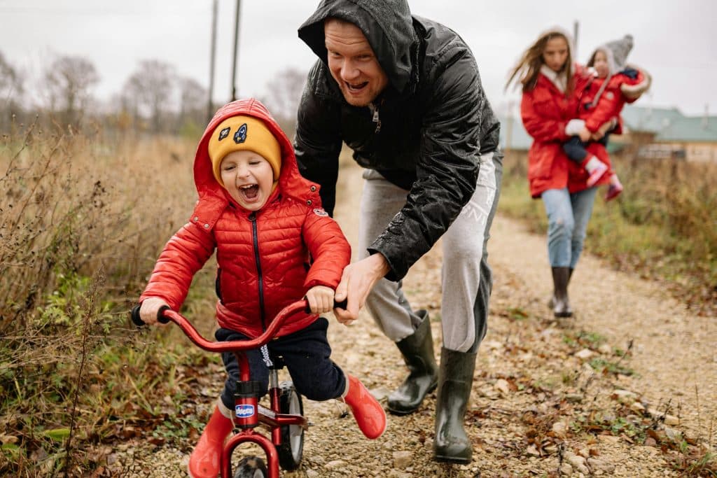 pexels photo 5792901 5792901 Father helping son ride a bicycle on a fall day while mother and daughter watch.