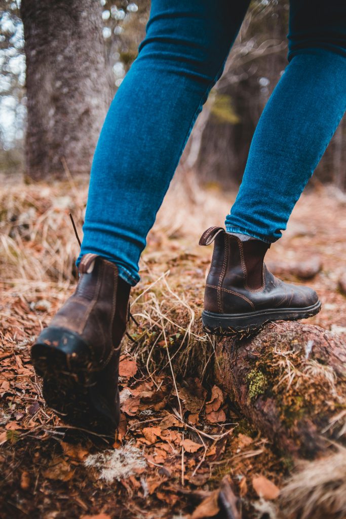 Close-up of a person hiking outdoors in a forest wearing denim jeans and leather boots.